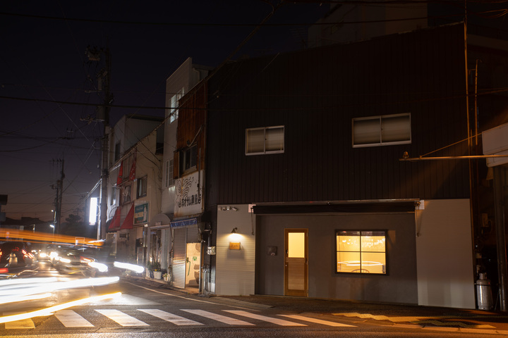 夜のまちなかに建つ一棟貸しの宿。窓から灯りがもれている(LifeStyleHotel ichi)